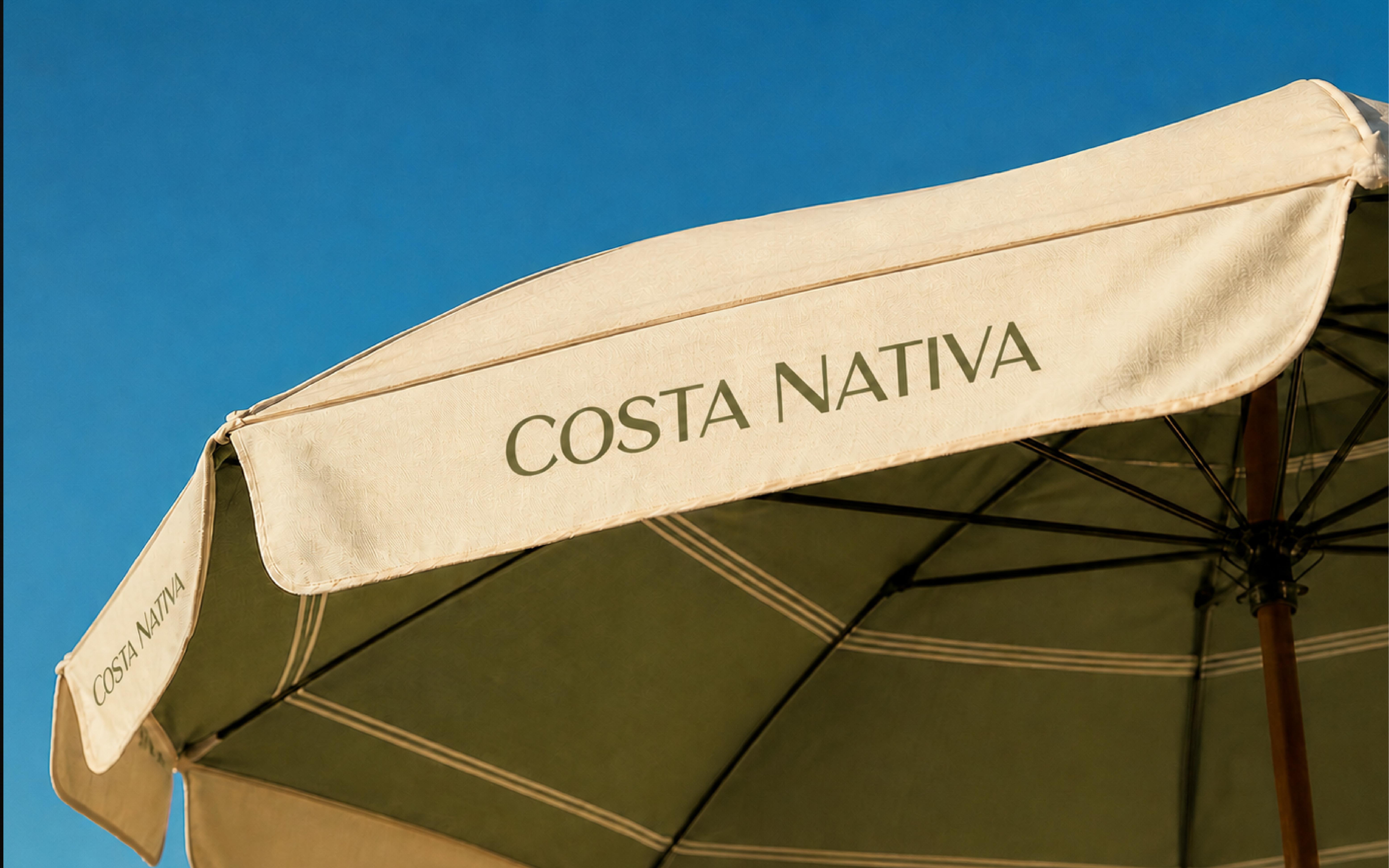 Sombrilla beige con texto Costa Nativa contra un cielo azul despejado.